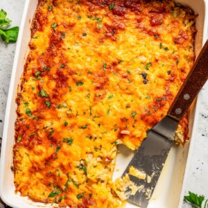 Overhead image of cheesy hash browns in a casserole dish with a slice taken out of them.