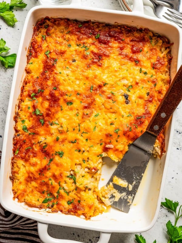 Overhead image of cheesy hash browns in a casserole dish with a slice taken out of them.