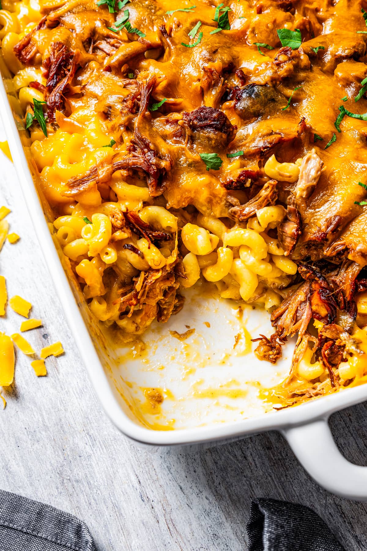 A casserole dish full of pulled pork mac and cheese with a serving of it pulled out of the dish.