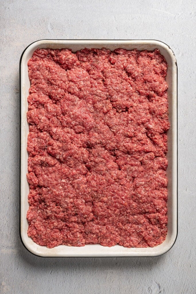 Pressing seasoned ground beef into a baking pan.