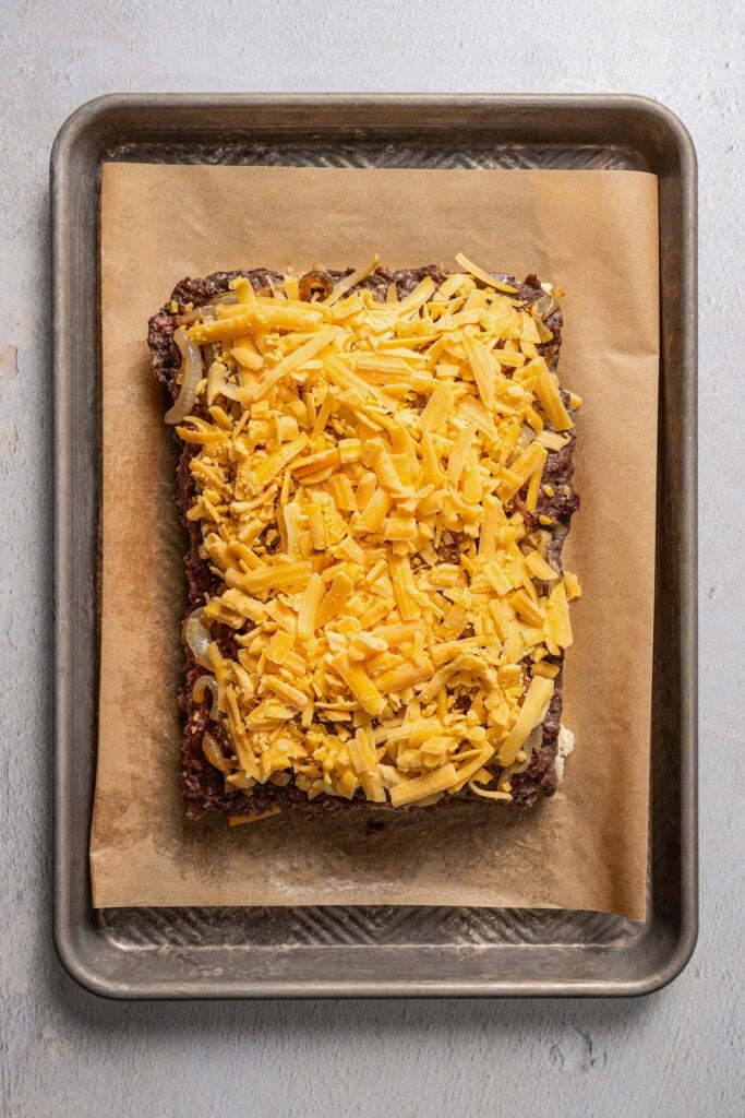 Topping a sheet of seasoned and cooked ground beef topped with caramelized onions with shredded cheddar cheese.