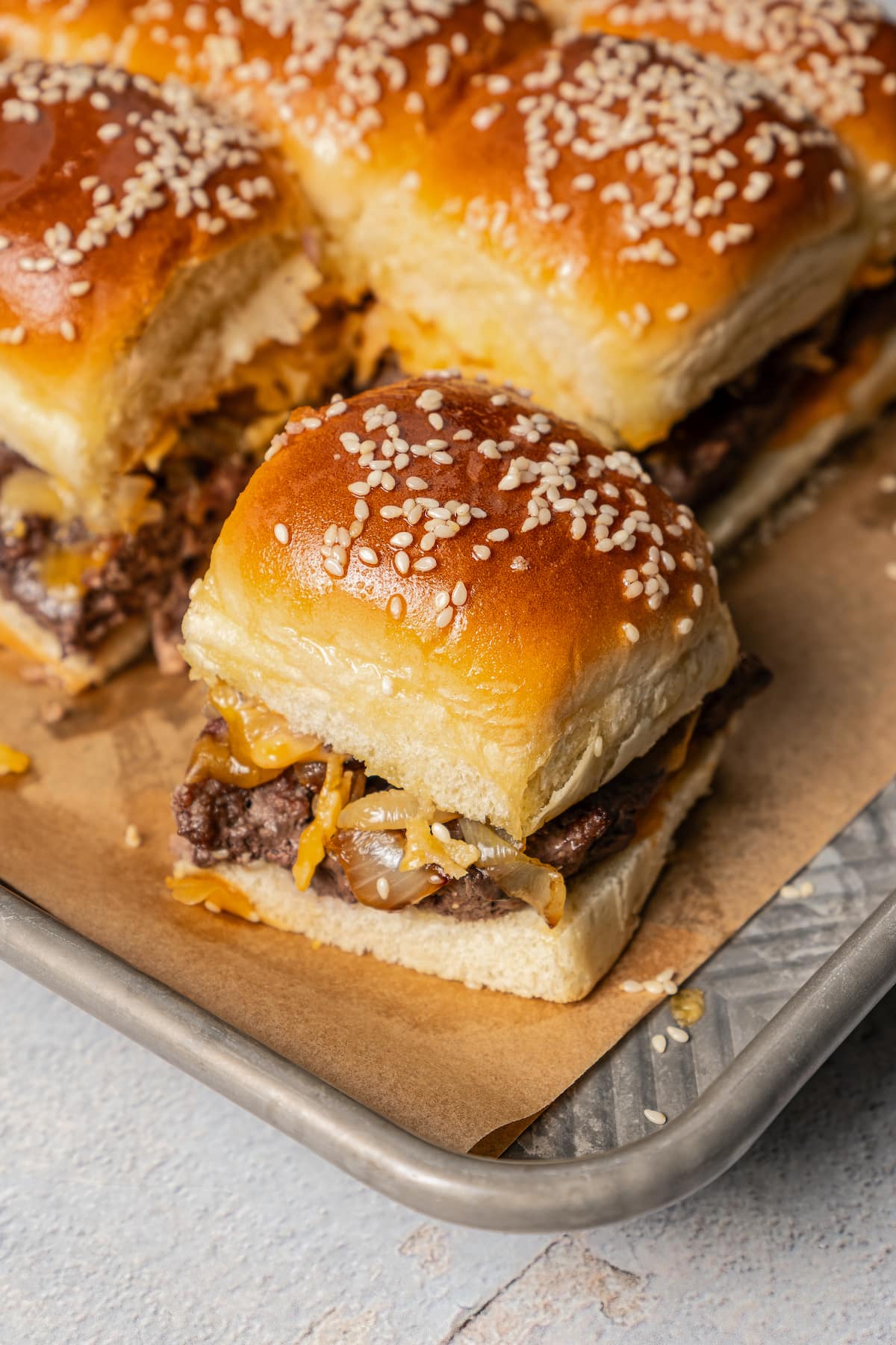 One cheeseburger slider cut away from a sheet pan full of them.