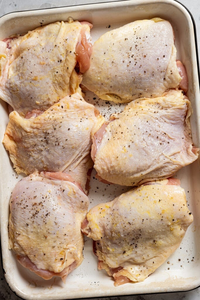 Seasoned chicken thighs in a baking pan.