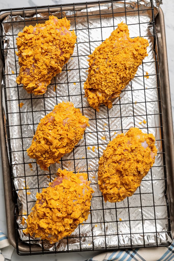Chicken thighs coated in cornflake breading on a wire rack over a baking sheet ready to go in the oven.