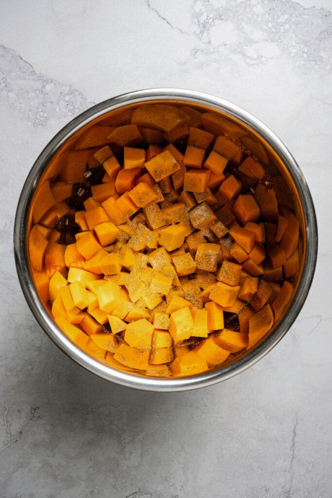 An Instant Pot loaded with sauteed shallots and garlic, cubed butternut squash, and seasonings.