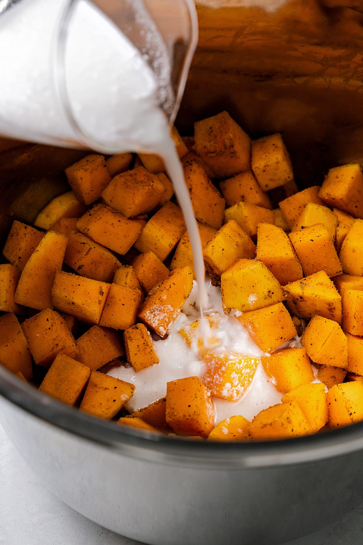 Pouring coconut milk into an instant pot with butternut squash, garlic, shallots, and seasonings.