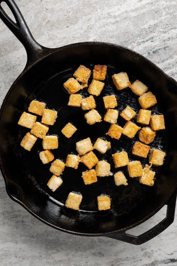 Tofu fried to golden-brown in a skillet.