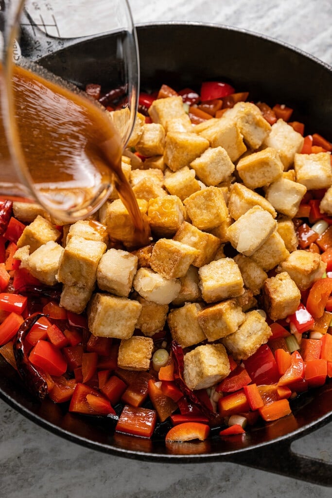 Adding tofu, sauce, peppercorns, and peanuts to a skillet full of sauteed veggies.