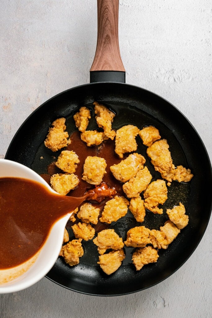 Pouring sauce over breaded and fried chicken pieces for sesame chicken.