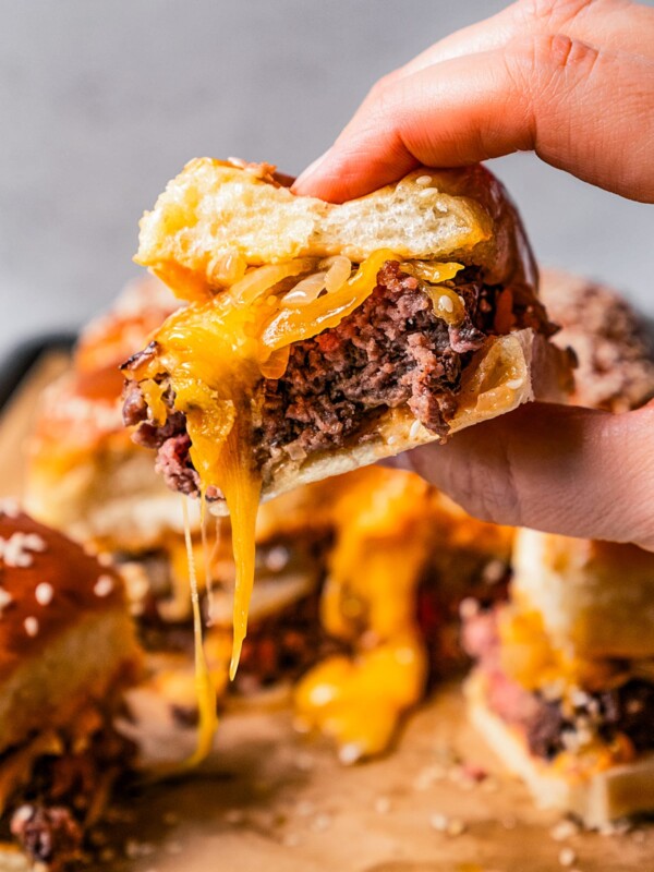 Female hand holding up a slider with melty cheese oozing out of it.