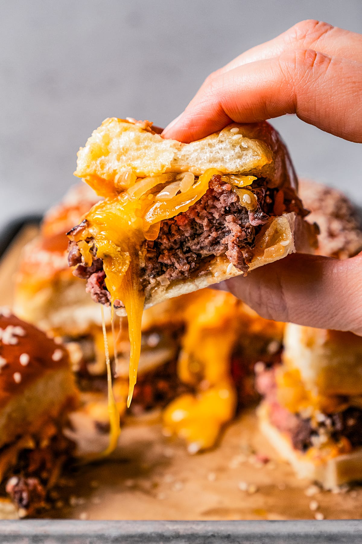 Female hand holding up a slider with melty cheese oozing out of it.