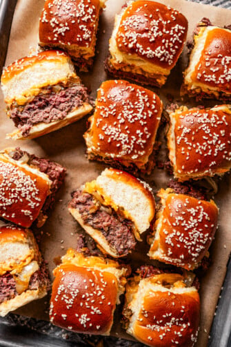 Cheeseburger sliders arranged on a sheet pan lined with parchment paper.