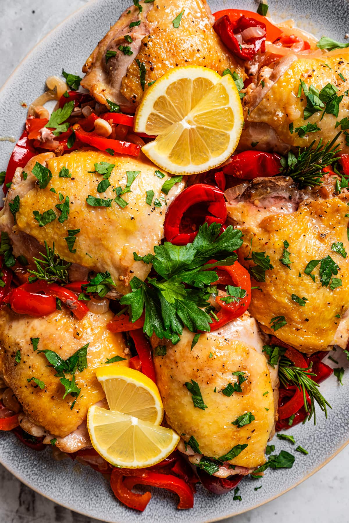 Chicken thighs served on a platter with julienne cut peppers, slices of lemons, and a garnish of parsley.