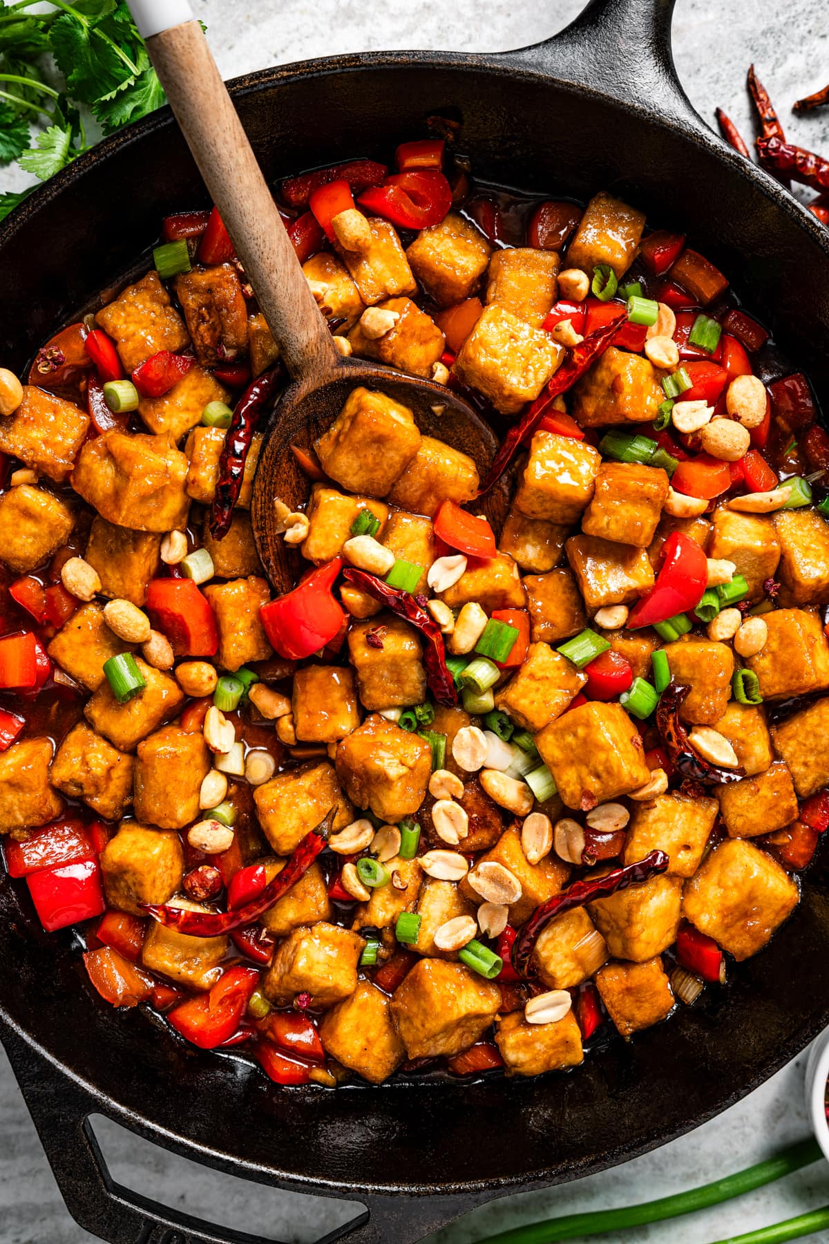 Kung pao tofu in a skillet with a wooden spoon stirring through it.