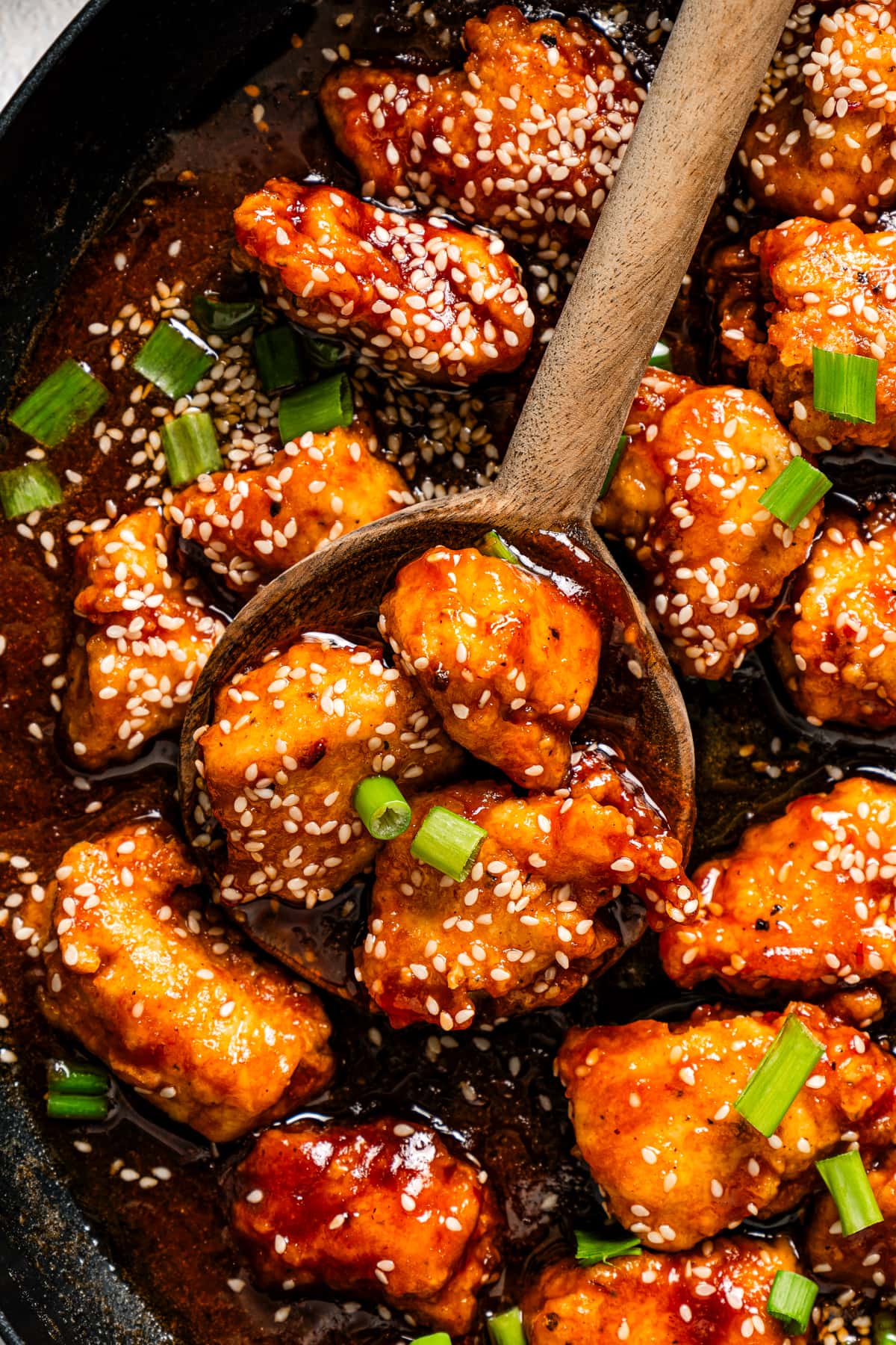 Close-up image of chicken cubes tossed in sweet and sour sauce and garnished with sesame seeds.