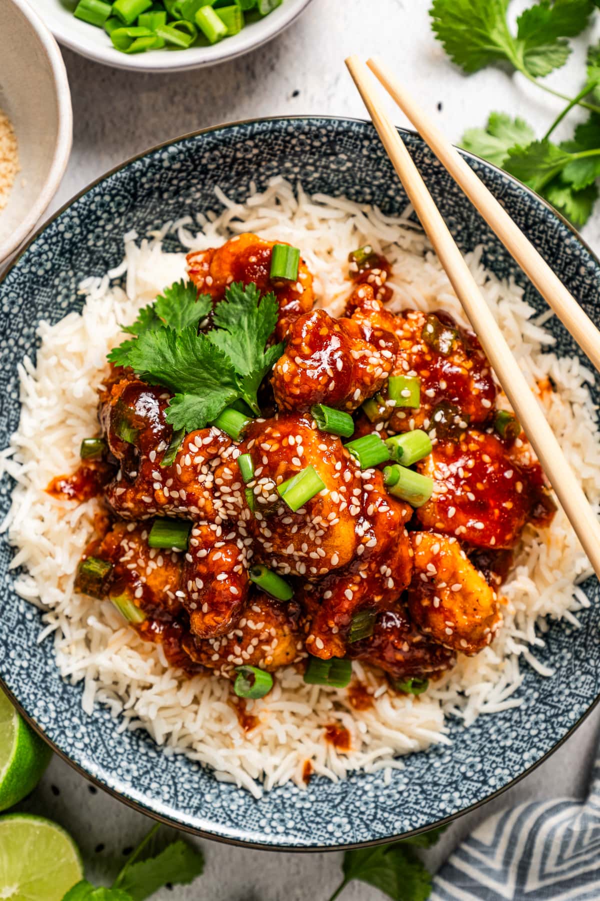 Overhead photo of sesame chicken served over white rice in a bowl with chopsticks.