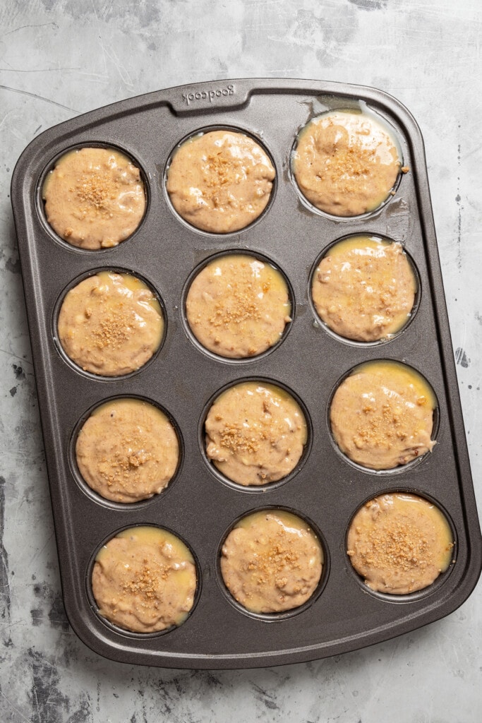 Filling a muffin pan with banana walnut muffin batter and topping with butter and raw cane sugar.