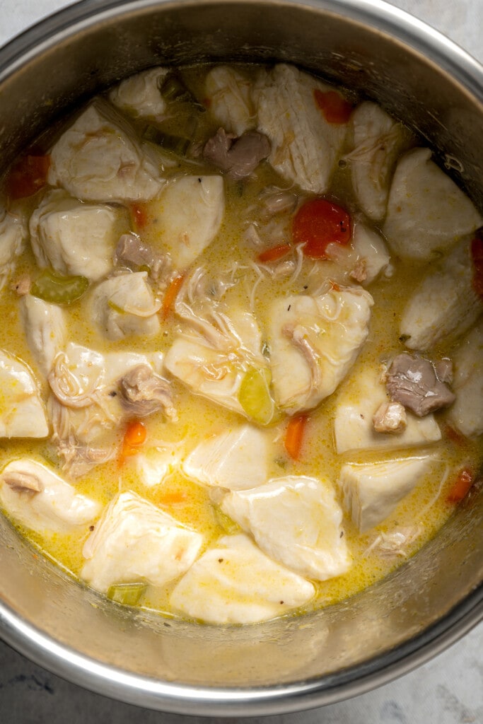 Adding quartered biscuits to an Instant pot full of chicken, veggies, and creamy broth.