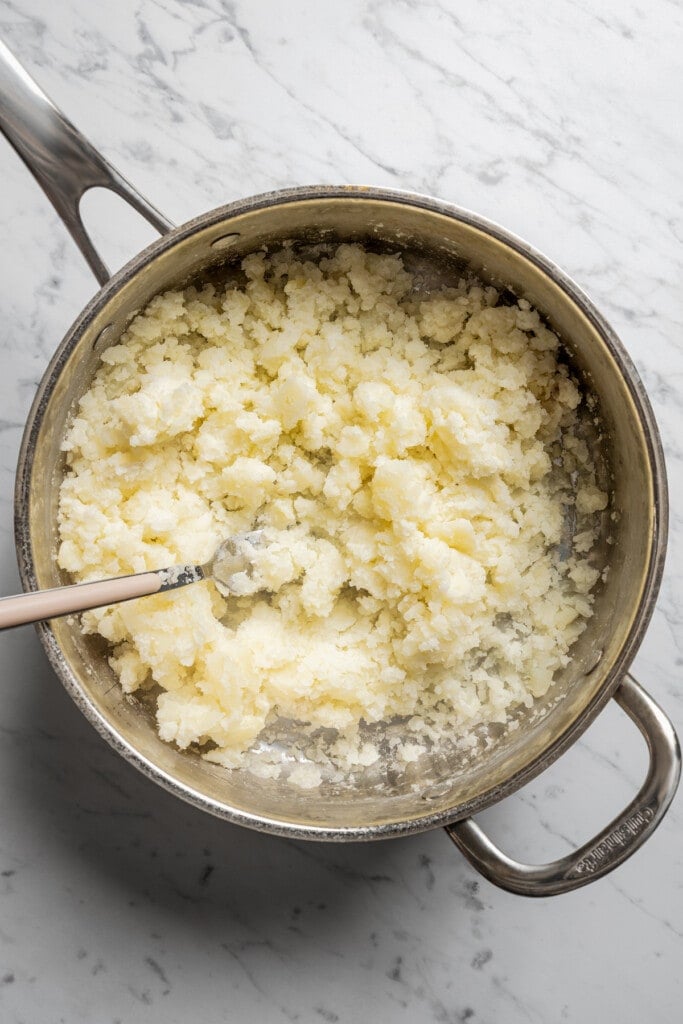 Mashing boiled russet potatoes with a fork.