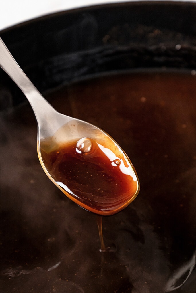 A spoon full of homemade teriyaki sauce hovering over a saucepan.