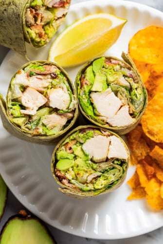 Closeup overhead image of chicken Caesar wraps on a plate with chips.
