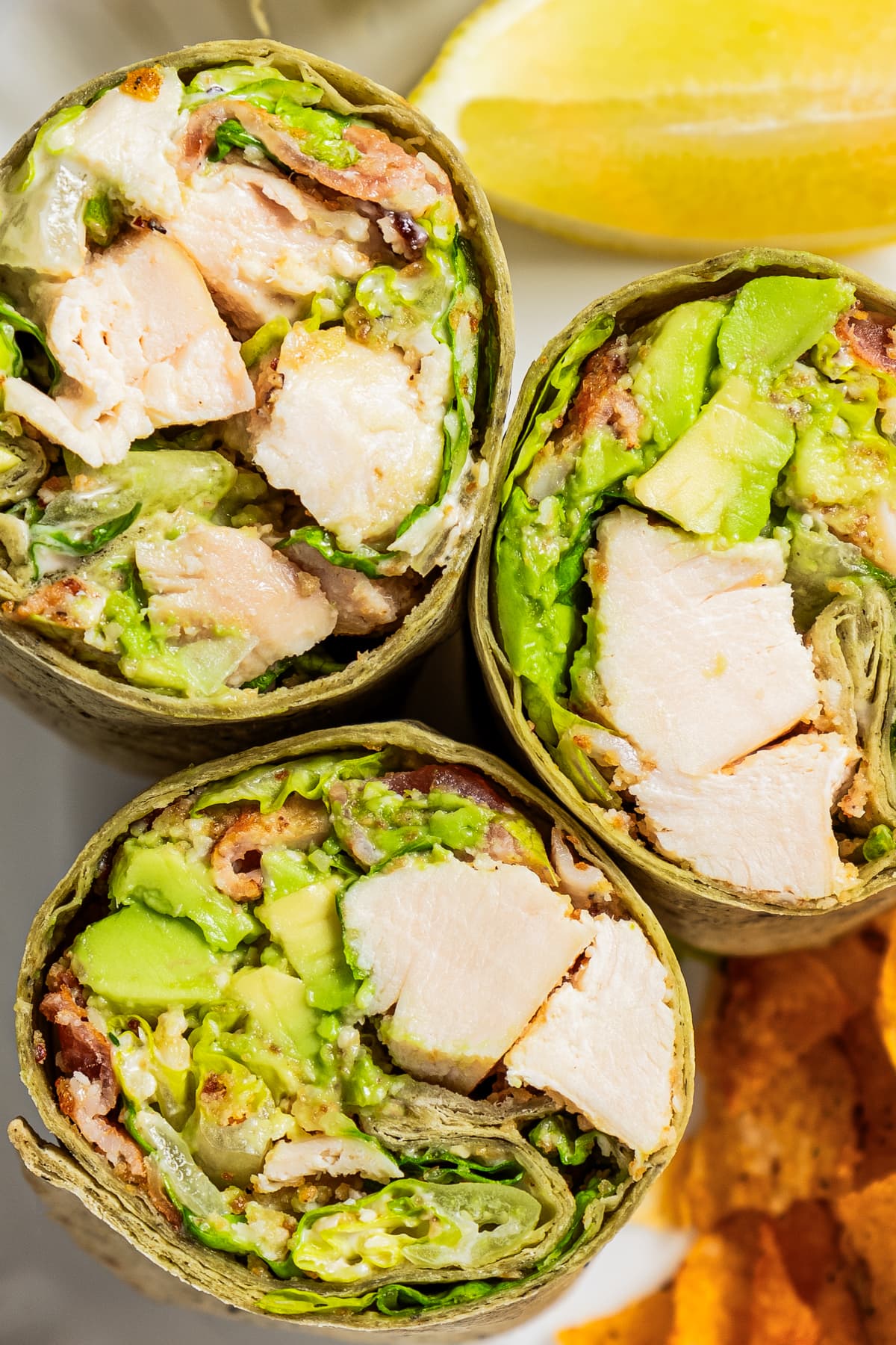Three chicken wraps cut in half with the filling exposed to view the ingredients inside the wrap.