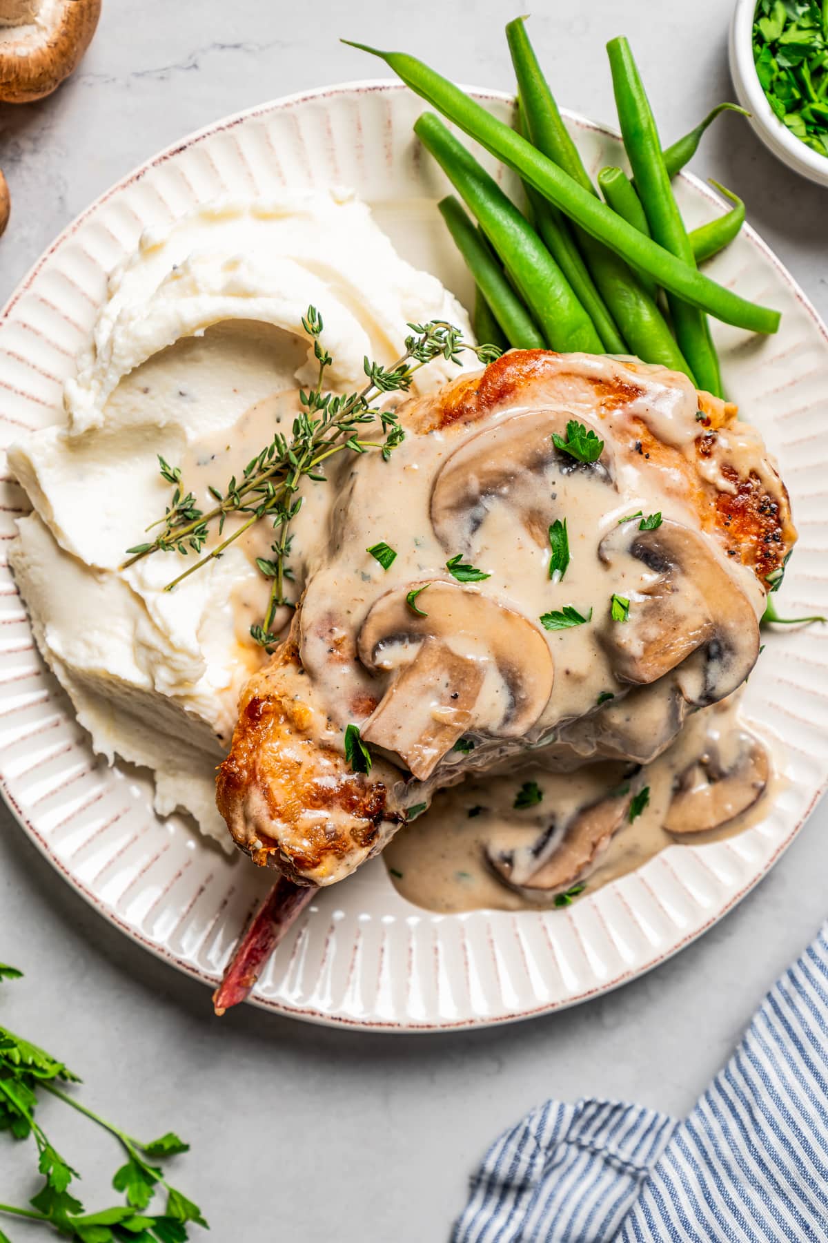 Dinner plate with a pork chop, mushroom sauce, mashed potatoes, and green beans.