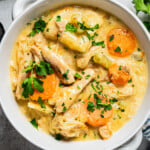 Chicken and dumplings served in a bowl and garnished with sliced carrots and chopped parsley.