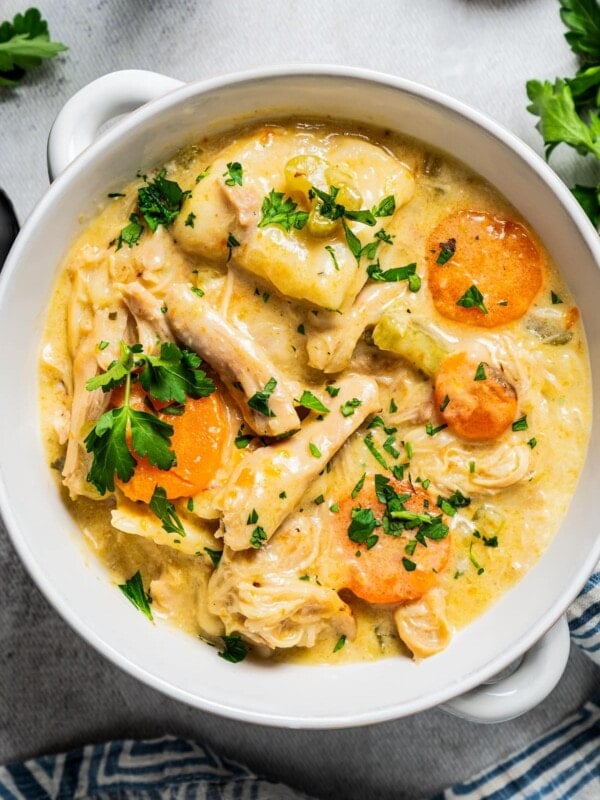 Chicken and dumplings served in a bowl and garnished with sliced carrots and chopped parsley.