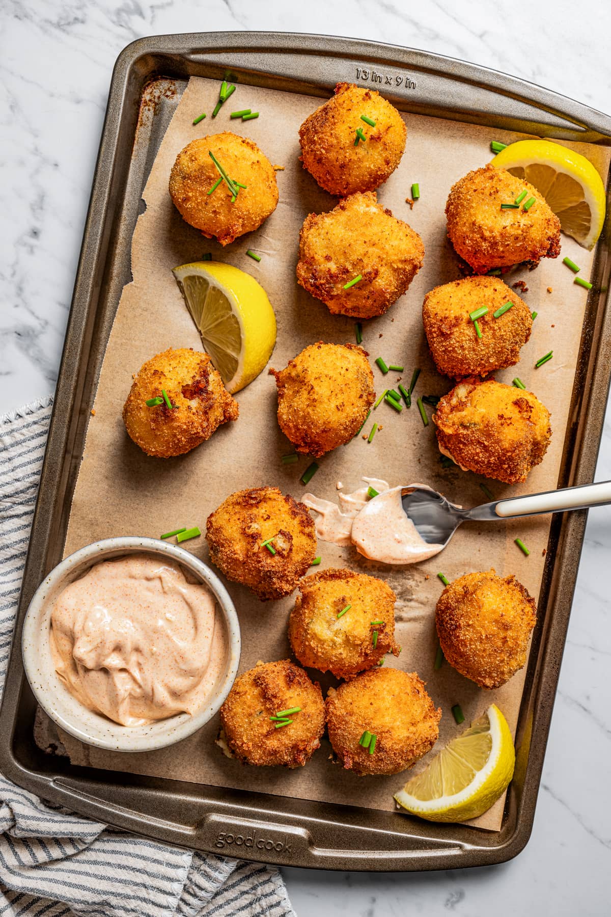 Potato croquettes on a baking sheet lined with parchment paper with a bowl of garlic aioli.