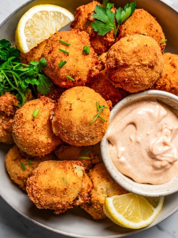 Close-up photo of potato croquettes served in a bowl with a side of aioli and lemon wedges.