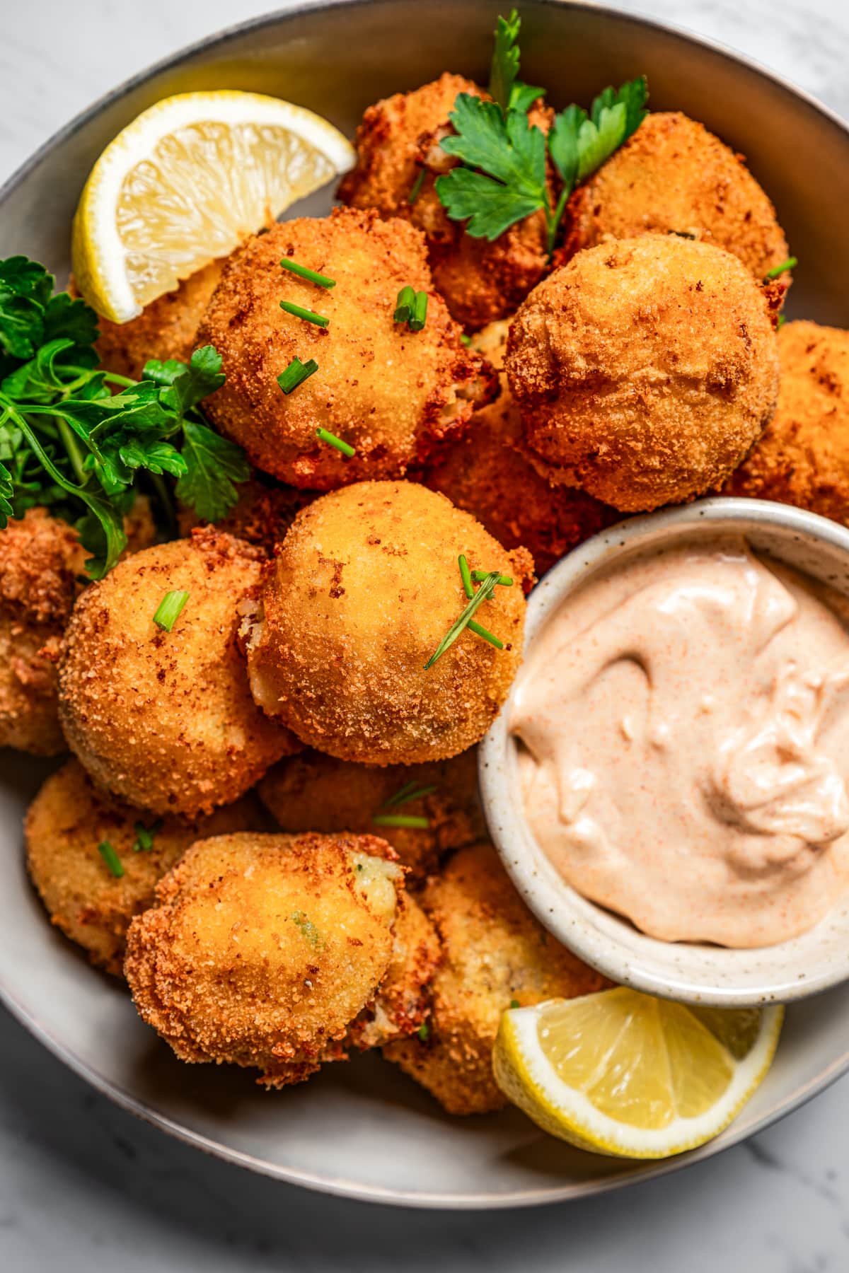 Close-up image of potato croquettes served in a bowl with garlic aioli and lemon wedges.