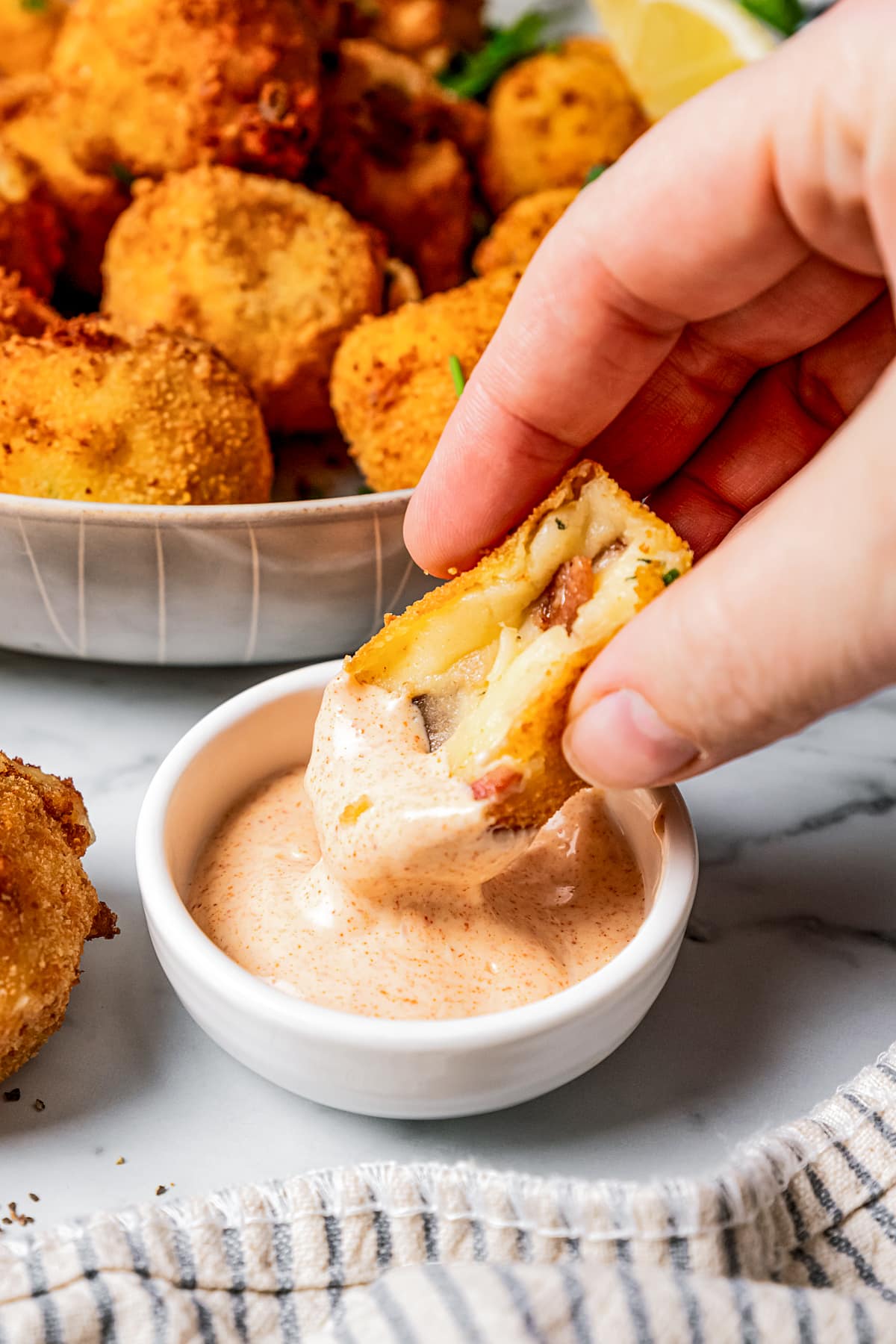 A potato croquette with a bite taken out of it and dipping it into garlic aioli.