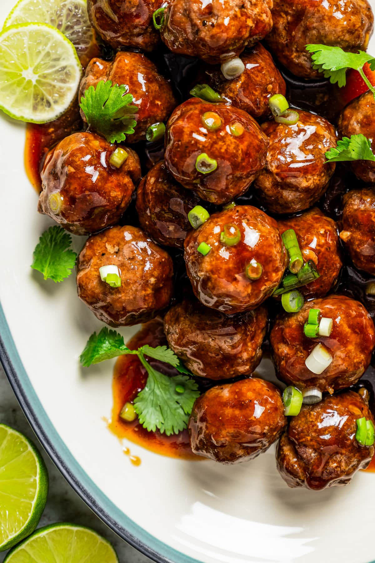 Close-up image of teriyaki meatballs arranged on a serving platter and garnished with herbs and green onions.