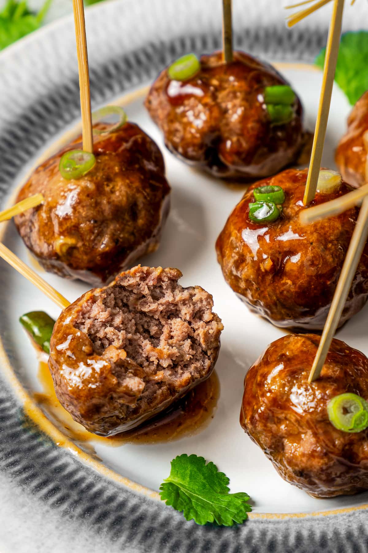 Meatballs skewered with toothpicks on a plate. One meatball has a bite taken out of it.