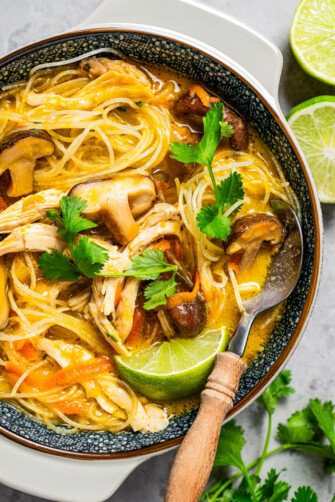 Thai chicken noodle soup served in a bowl and garnished with lime and herbs.
