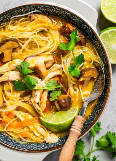 Thai chicken noodle soup served in a bowl and garnished with lime and herbs.