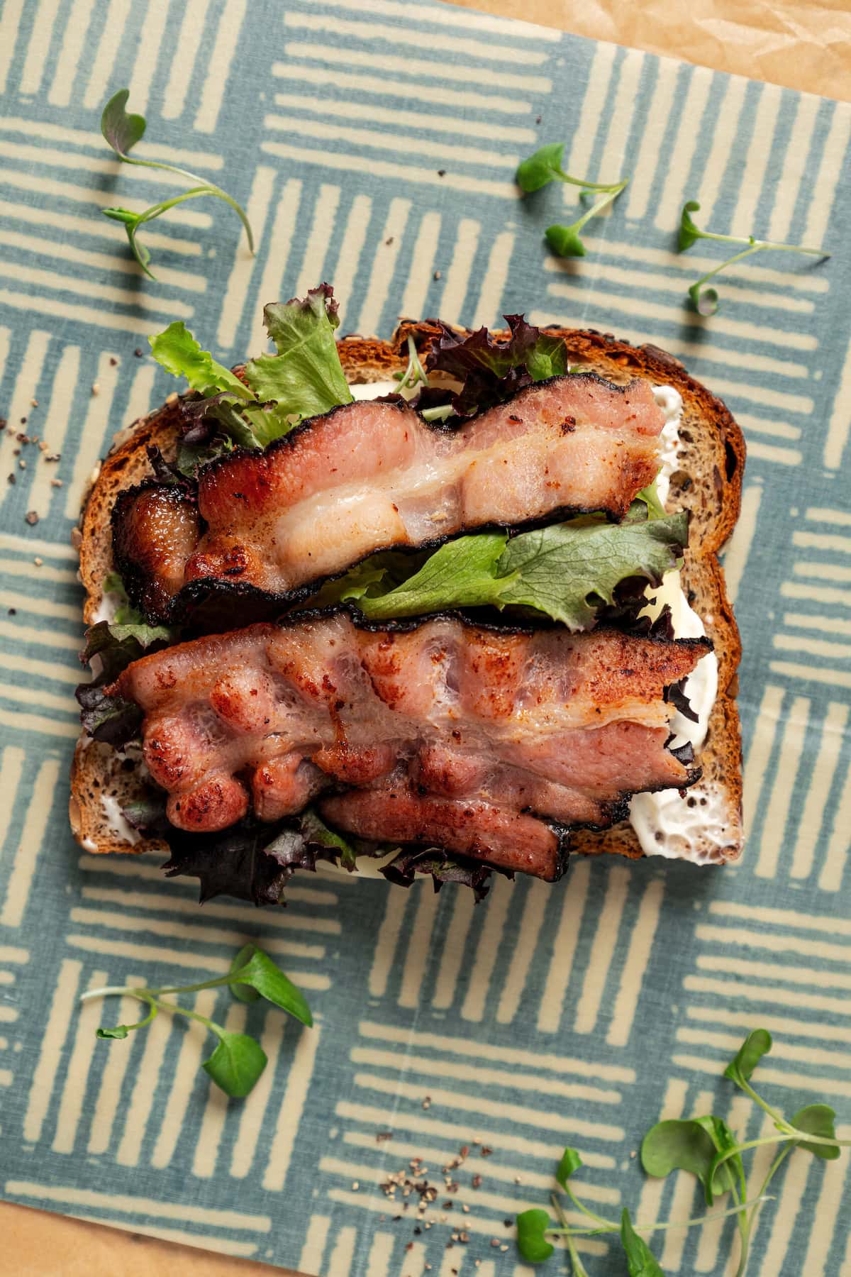 Layering lettuce and crispy bacon over a piece of bread smothered in mayo.