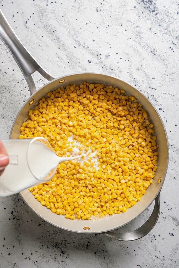 Pouring heavy cream into a saucepan full of corn.