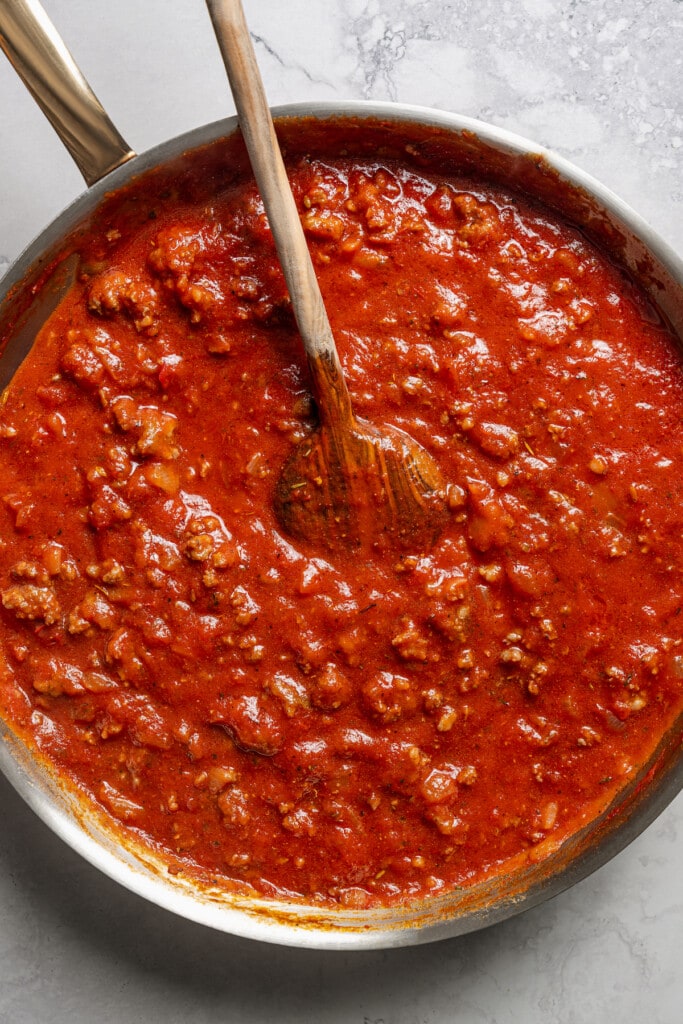 Meat sauce in a skillet with a wooden spoon.