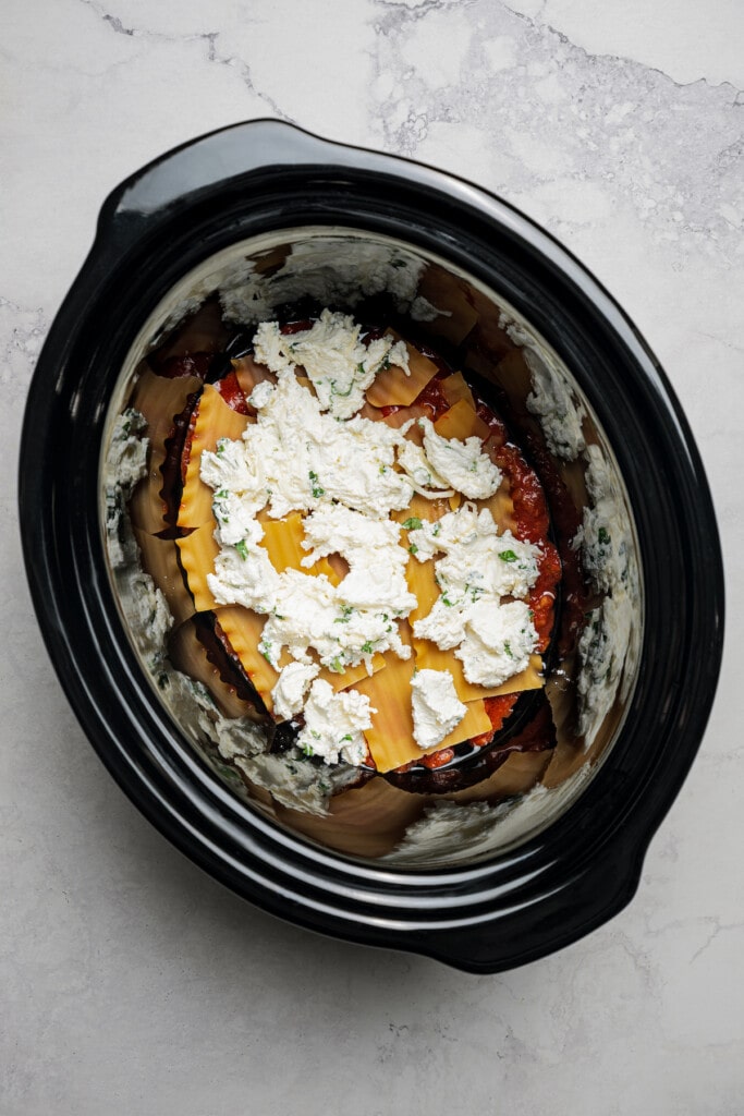 Adding a layer of cheese to crockpot lasagna.
