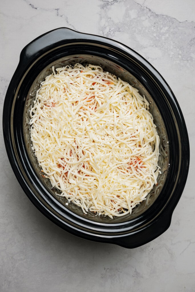 Sprinkling cheese over crockpot lasagna.