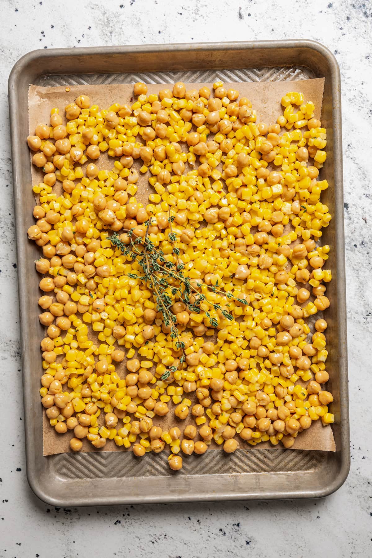 Spreading seasoned corn and garbanzo beans out on a baking dish with thyme.