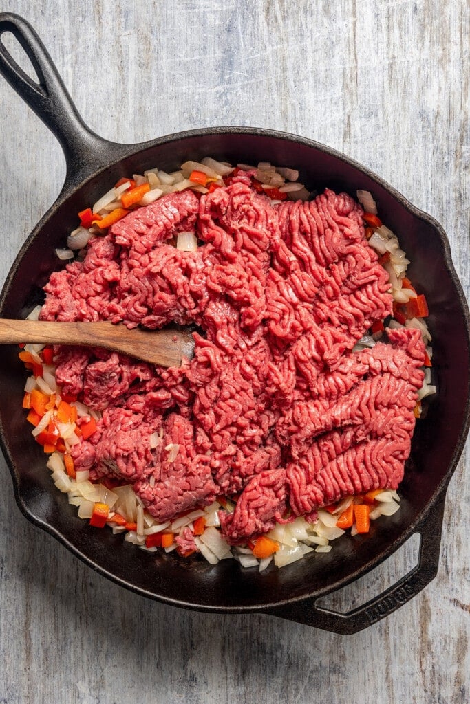 Cooking ground beef in a skillet with sauteed onion, bell pepper, and garlic.