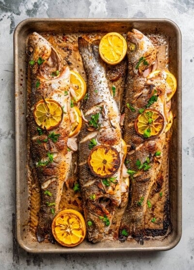 Overhead image of three roasted branzino fish on a sheet pan with lemon slices.