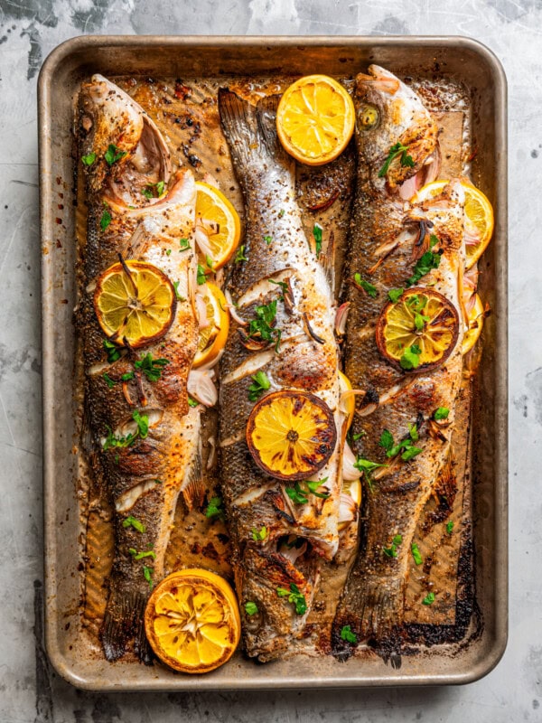 Overhead image of three roasted branzino fish on a sheet pan with lemon slices.