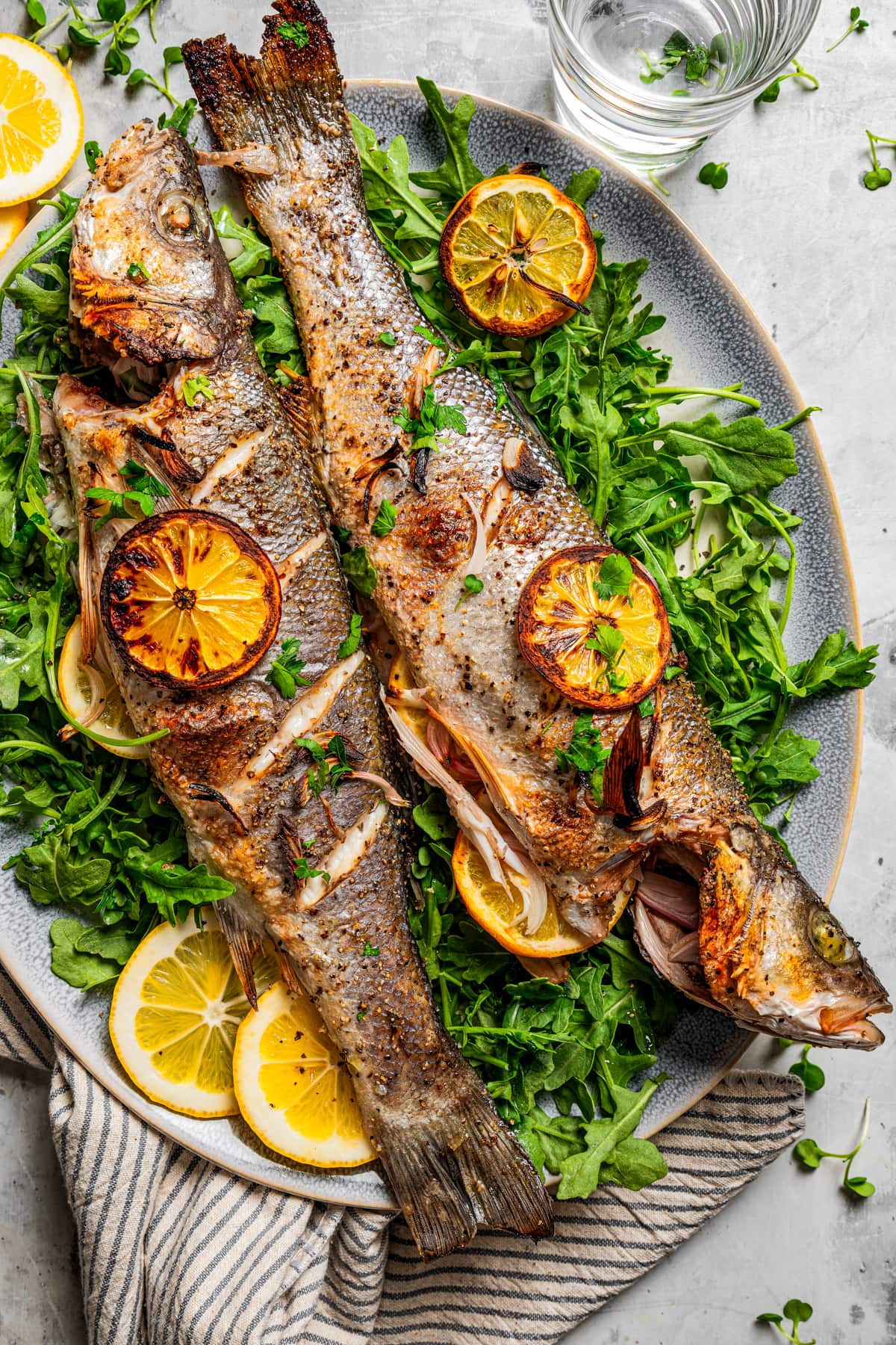 Branzino served on a serving platter and garnished with lemon slices and green herbs.