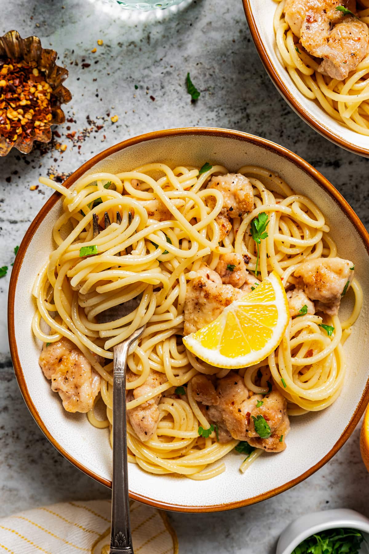 Pasta and chunks of chicken served in a plate and garnished with a slice of lemon.