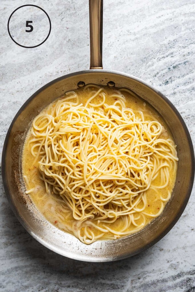Tossing spaghetti with butter sauce in a skillet.