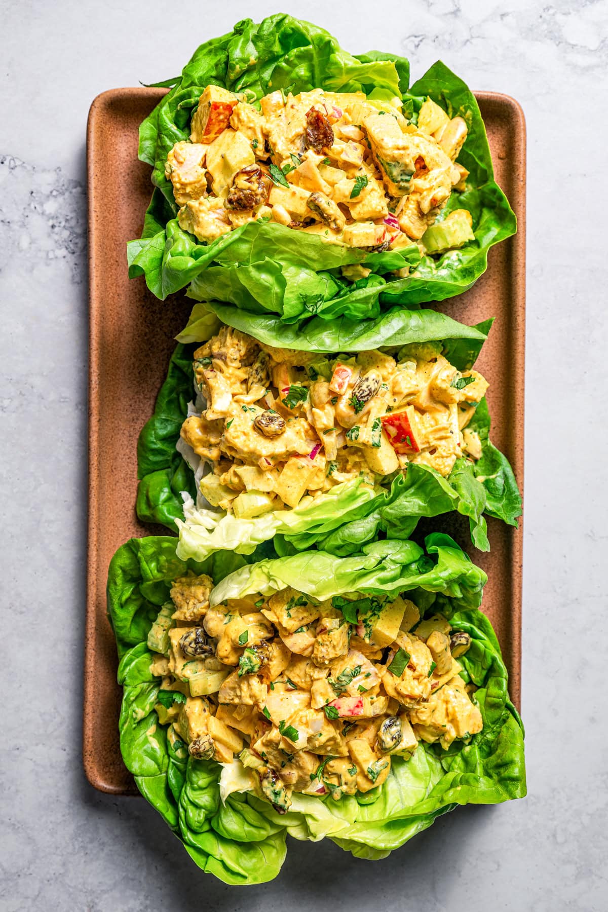 Three lettuce wraps with chicken salad arranged on a wooden board.